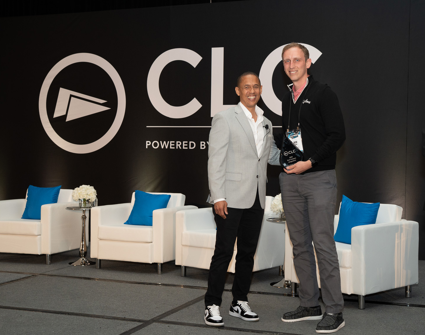 Two people standing on a stage accepting an award and smiling at the camera.