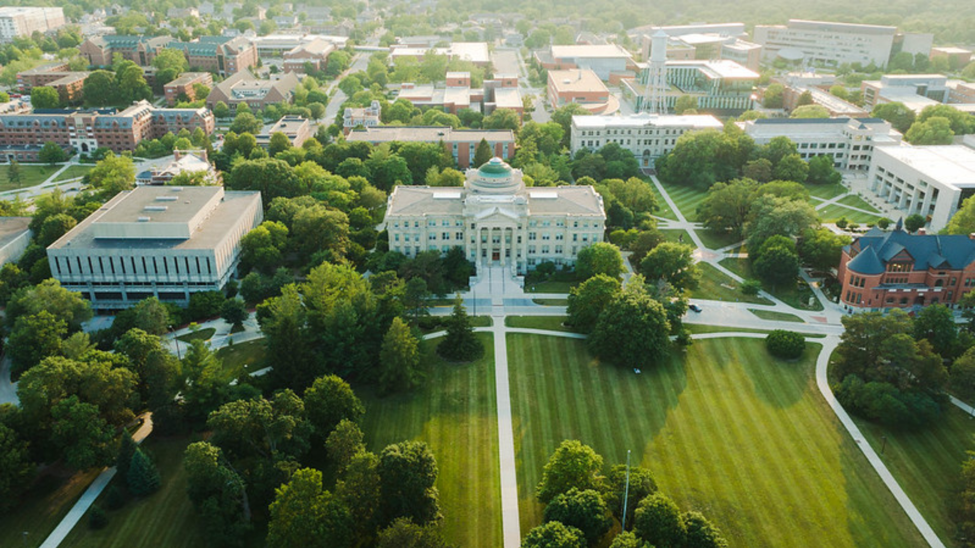 Aerial view of a campus with a domed building, tree-lined walkways, and green lawns surrounded by academic buildings.